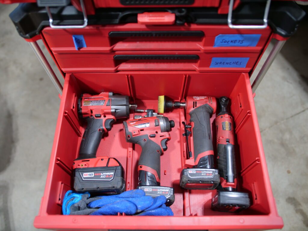 Close-up of a Milwaukee Packout drawer showcasing a selection of cordless power tools, including impact drivers, ratchets, and a drill.