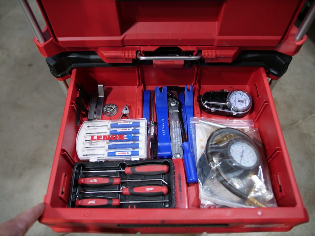 Close-up of a Milwaukee Packout drawer showcasing various precision tools, including picks, Lenox precision screwdrivers, a compression tester, a low-pressure tire gauge, feeler gauges, and plastic removal tools.