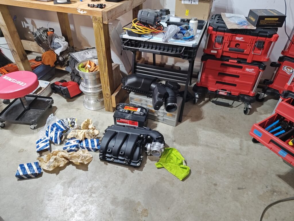 Garage workspace showing Ford Taurus intake manifold, spark plug boxes, and Milwaukee Packout storage system