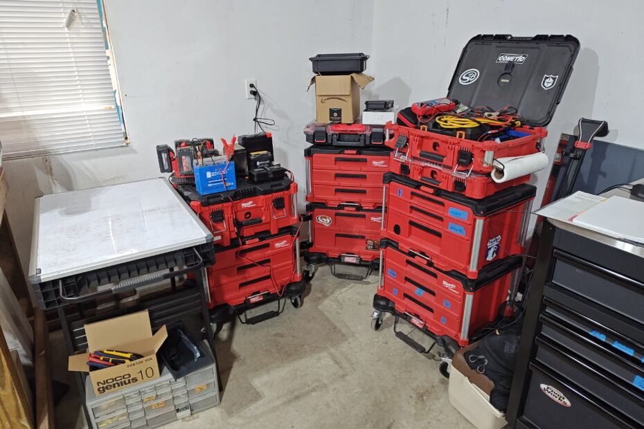 Organized Milwaukee Packout storage system in a workshop, featuring modular toolboxes, battery maintenance tools, and a Noco Genius 10 charger on a table.